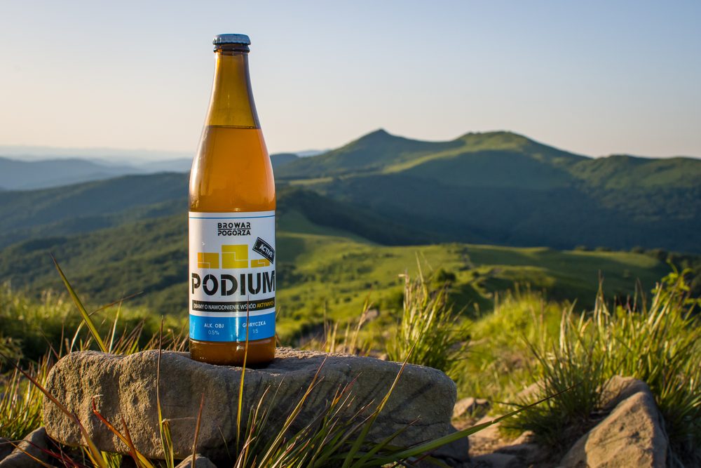 Butelka bezalkoholowego piwa Podium 0,5% Browaru Pogórza na skale na tle gór